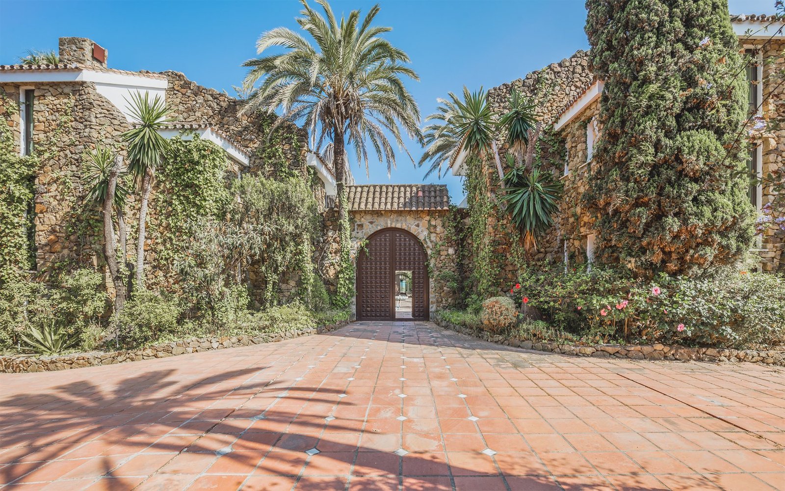 Arched timber gate in a stone courtyard wall, terracotta forecourt in the foreground